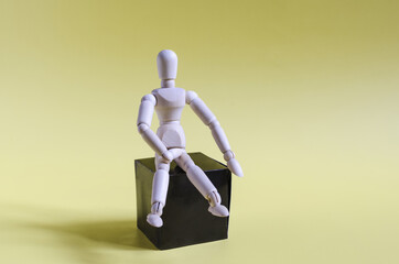 The figure of a wooden man sitting on a dark podium. The figure of a wooden man on a yellow background of the mine space.