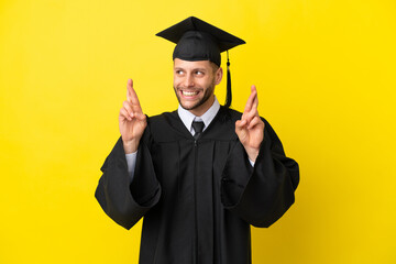 Young university graduate caucasian man isolated on yellow background with fingers crossing