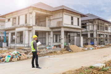 young professional engineer in protective helmet and blueprints paper at the house building construction site