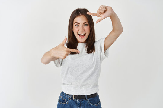 Young beautiful blonde woman with blue eyes wearing casual t-shirt over white background smiling making frame with hands and fingers with happy face. Creativity and photography concept