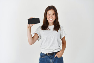 Young beauty woman holding blank screen mobile phone and smiling, showing smartphone display...
