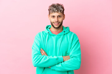 Young handsome caucasian man isolated on pink background keeping the arms crossed in frontal position