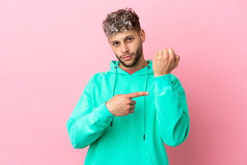 Young handsome caucasian man isolated on pink background making the gesture of being late