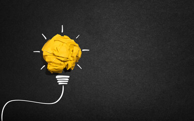 creative Idea, yellow crumpled paper ball shaped like an electric bulb on black paper or blackboard