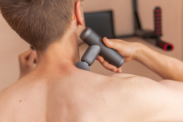A young man is using and enjoying percussion massage gun to relax and relief the pain in body and muscles 