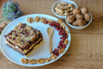 Piece of tasty chocolate-nut cake on a white plate. Walnuts and wooden spoon stand nearby