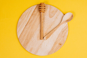 Clock is in on a wooden surface. Lunch time concept. On a yellow background