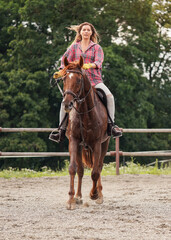 Obraz premium Young woman wearing shirt riding brown horse in sand paddock by wooden fence, hair moving in air because of speed
