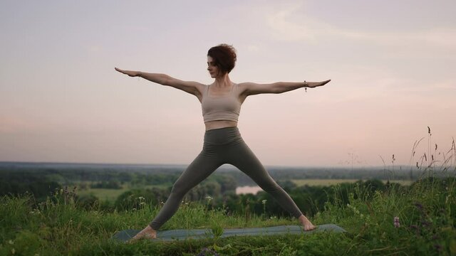 Young woman preforms yoga in mountains in morning light. Woman performs yoga moves on mountain summit. Serenity and yoga practicing at mountain range,meditation