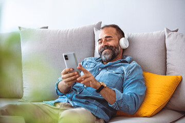 Time to relax. Handsome middle-aged bearded man in wireless headphones listening to music online on...