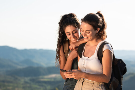 Cheerful women using smartphone on sunny hilly terrain