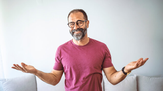 Portrait of happy mature man wearing spectacles and looking at camera indoor. Man with beard and glasses feeling confident.  Handsome mature man posing against a grey background