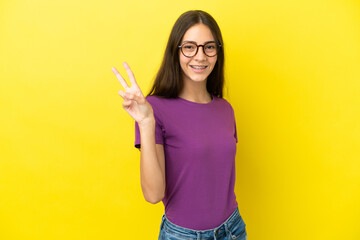 Young French woman isolated on yellow background smiling and showing victory sign