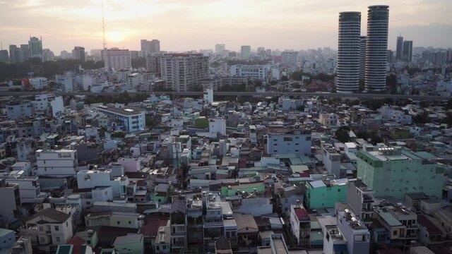 Different old small buildings surround large skyscrapers under bright sunlight and orange white sky at sunrise aerial view. Ho Chi Minh City, Vietnam.