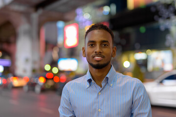 Portrait of handsome black African businessman outdoors in city at night smiling