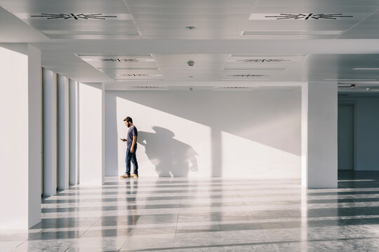 Man standing in empty spacious office hall and browsing smartphone