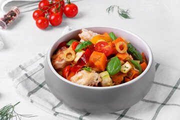 Salad with baked vegetables, croutons, olives, capers, cherry tomatoes, basil and olive oil served in the gray bowl. Mediterranean meal