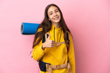 Young mountaineer girl with a big backpack isolated on pink background giving a thumbs up gesture