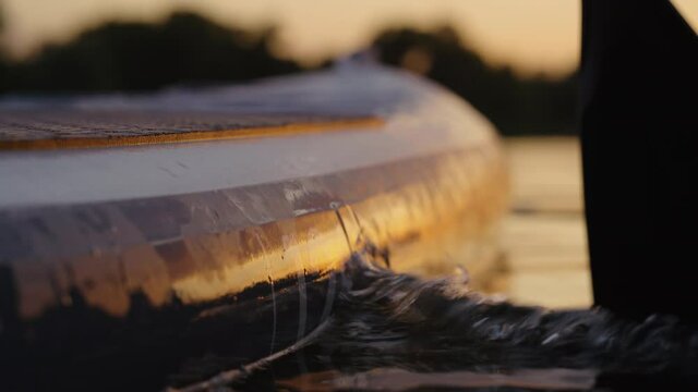 Paddling on SUP board in rays of sunset. Closeup of aquatic sports in summer. Healthy lifestyle and outdoor activity. Concept of vacation