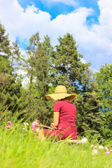 Plein air. A woman in a straw hat is drawing blooming peonies in a summer park.