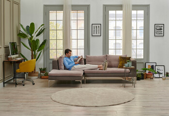 Man is reading a book in the decorative living room style, grey sofa working table background home...