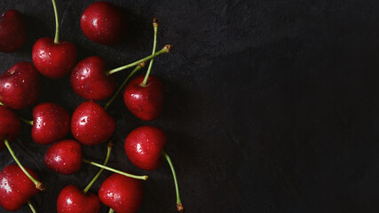 Cherry tree macro black background top view. Ripe juicy cherry berries in drops of water are lying on the table. The concept of freshness, proper nutrition, vitamins. Low key photo. Copy space