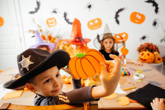 Cute boy in cowboy hat demonstrates his handmade paper pumpkin
