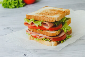Close-up photo of a club sandwich. Sandwich with meat, prosciutto, salami, salad, vegetables, lettuce, tomato on a ​​rye bread on wooden background