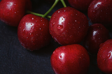 Cherry tree macro black background top view. Ripe juicy cherry berries in drops of water are lying on the table. The concept of freshness, proper nutrition, vitamins. Low key, close-up. Copy space