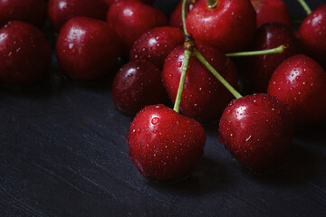 Cherry tree macro black background top view. Ripe juicy cherry berries in drops of water are lying on the table. The concept of freshness, proper nutrition, vitamins. Low key, close-up. Copy space