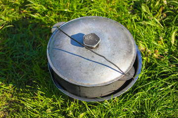 Camping gray aluminum cauldron on a green grass on a sunny summer day flatly. Cooking in nature during a camping trip. Traveling, tourism, picnic cooking, cooking at the stake in a cast iron cauldron.