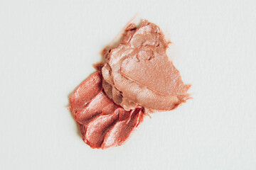 A smear of nude lipstick with shimmery particles on a light background. Cosmetic texture