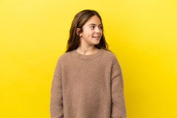 Little caucasian girl isolated on yellow background looking side