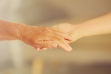 Helping hands on blurred background, closeup. Elderly care concept