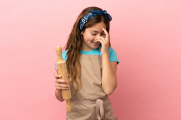 Little caucasian girl holding a rolling pin isolated on pink background laughing