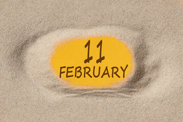 February 11. 11th day of the month, calendar date. Hole in sand. Yellow background is visible through hole. Winter month, day of the year concept