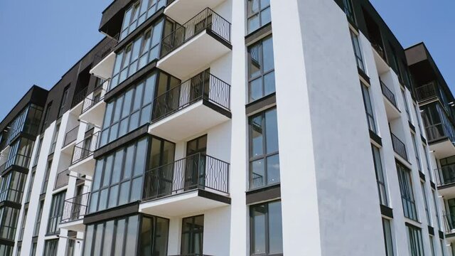 Block of flats on sky background. Modern high-rise apartment building with windows and large balconies. Camera rising up.
