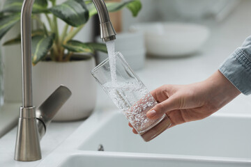 Woman filling glass with water from tap in kitchen, closeup - Powered by Adobe