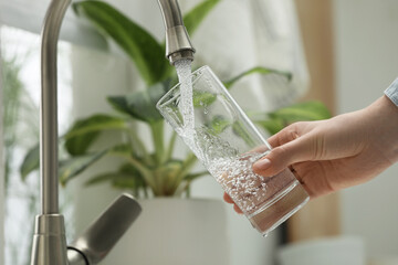 Woman filling glass with water from tap at home, closeup