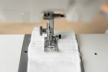Sewing machine with with a white cloth on a wooden table.
