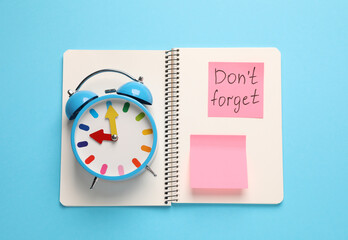 Alarm clock, notebook and reminder note with phrase Don't forget on light blue background, top view