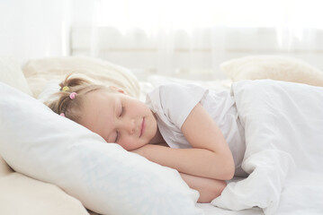 Obraz na płótnie Canvas A cute little girl enjoys an afternoon nap in bed after dinner