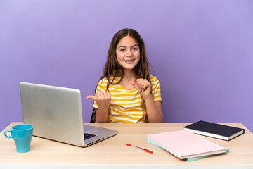 Naklejka premium Little student girl in a workplace with a laptop isolated on purple background pointing to the side to present a product