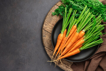 Fresh carrots on a board on a brown background. Top view, copy space.
