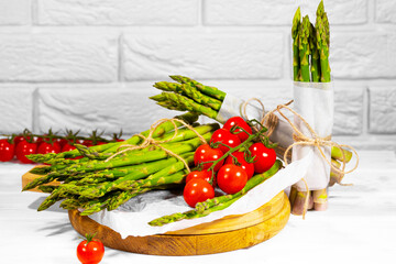 Green Asparagus ant Tomato on wooden board on white brick Background. Healthy eating. Alkaline Food