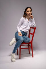 Young woman in a white shirt and jeans on a red chair.