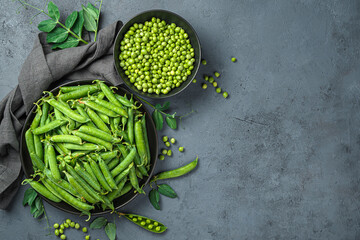 Pea pods and peeled peas on a dark gray background with space for copying. Top view, horizontal.