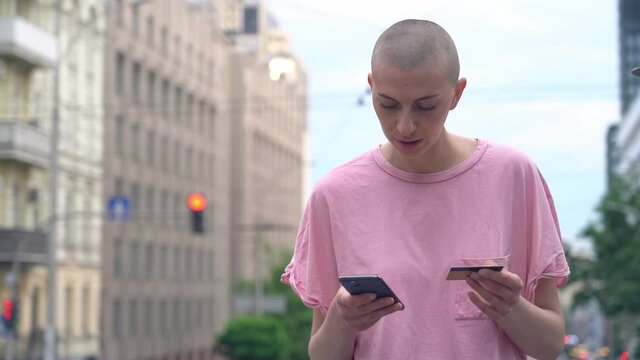 Pensive woman holding credit card, using smartphone for online shopping, mobile banking standing on the street
