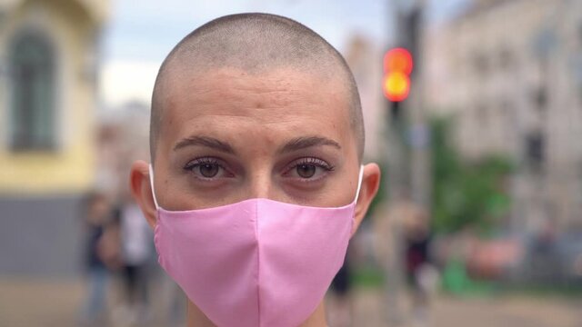 Bald Woman in protective face mask looking at camera standing on the street. Coronavirus, health care concept