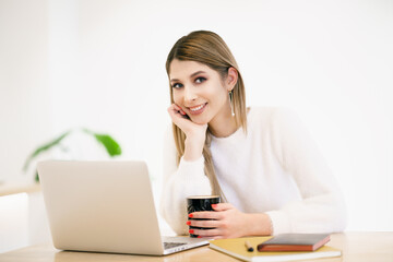 Beautiful young woman in casual clothing using laptop and smiling while working indoors